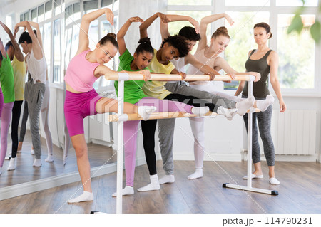 Teenage girl doing leg stretching exercise holding by ballet barre during dance courses 114790231