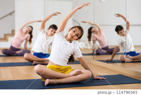 Girl doing Padmasana with side stretch during family yoga workout 114790365