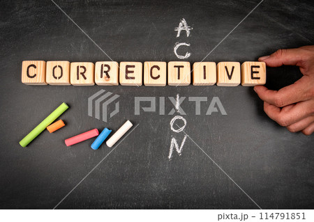 Corrective action. Wooden block crossword puzzle and pieces of chalk on a chalkboard background 114791851