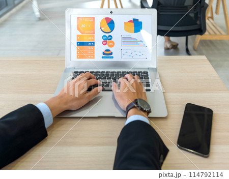 Back view of businessman in black suit sit at desk in office typing on laptop computer keyboard, making presentation with graph and multicolored chart. Back view of businessman in black suit sit at desk in office typing on laptop computer keyboard, making presentation with graph and multicolored chart. 114792114