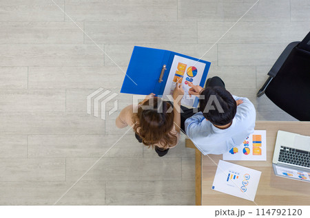 Two people are looking at chart and graph during a meeting from a top-down view. 114792120