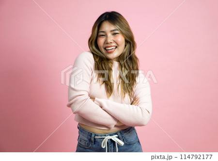Happy woman in pink sweater and jean stand with arms crossed and smiling. Portrait on a simple pink background with studio light. 114792177