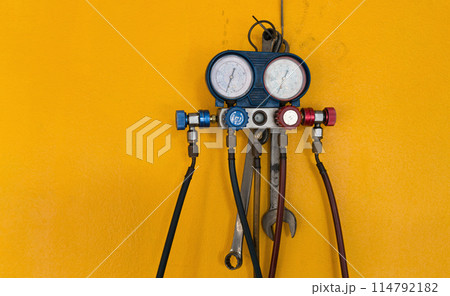 Manifold Gauge with hoses and a wrench on a yellow wall. Manifold Gauge with hoses and a wrench on a yellow wall. 114792182