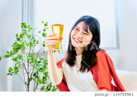 自宅の部屋で休日の明るい時間帯からグラスに入れられたビールを飲んで味わう20代から30代の若い女性 自宅の部屋で休日の明るい時間帯からグラスに入れられたビールを飲んで味わう20代から30代の若い女性 114793961