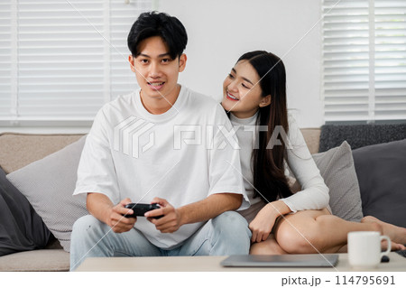 A man and woman are sitting on a couch playing a video game. The man is holding a controller and the woman is leaning on him. Scene is relaxed and playful A man and woman are sitting on a couch playing a video game. The man is holding a controller and the woman is leaning on him. Scene is relaxed and playful 114795691