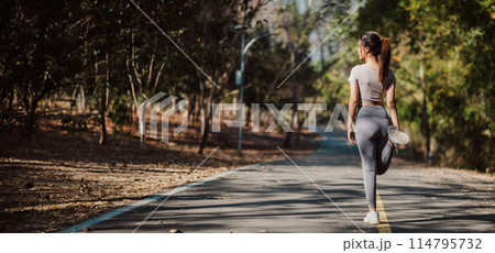 A woman is walking on a road with her legs spread apart. She is wearing a grey shirt and grey pants 114795732