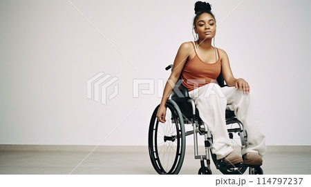 Young disabled African American woman in wheelchair against white wall 114797237