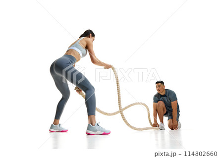 Dynamic photo of athletic woman and man engaged in workout with battle ropes against white studio background. Dynamic photo of athletic woman and man engaged in workout with battle ropes against white studio background. 114802660