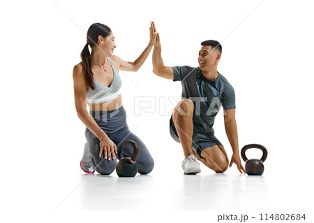 Portrait of man and woman taking break from their workout, kneeling on floor and give high five against white studio background. 114802684