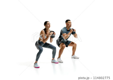 Man and woman exercising with kettlebells in squat position against white studio background. Athletic movements. 114802775