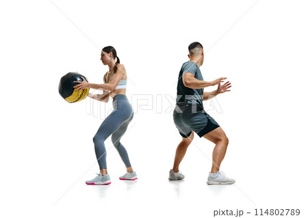 Pair of athletes engaged in dynamic exercise involving large black medicine ball against white studio background. Pair of athletes engaged in dynamic exercise involving large black medicine ball against white studio background. 114802789