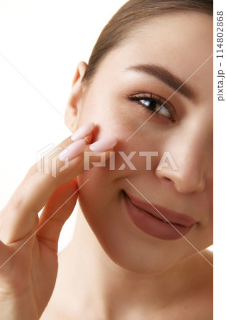 Close-up photo of young brunette woman with moisturized, smoothy skin and neutral make up touches skin against white background. 114802868