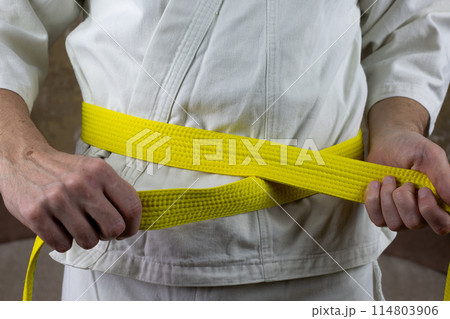 Kyokushinkai karate athlete ties yellow belt around his waist, adjusting martial arts equipment, senior student yellow belt Kyokushinkai karate athlete ties yellow belt around his waist, adjusting martial arts equipment, senior student yellow belt 114803906