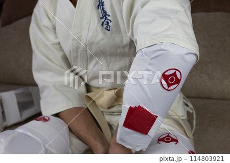 Kyokushinkai karate athlete wears elbow protection, protective equipment for martial arts sparring, health protection in karate Kyokushinkai karate athlete wears elbow protection, protective equipment for martial arts sparring, health protection in karate 114803921