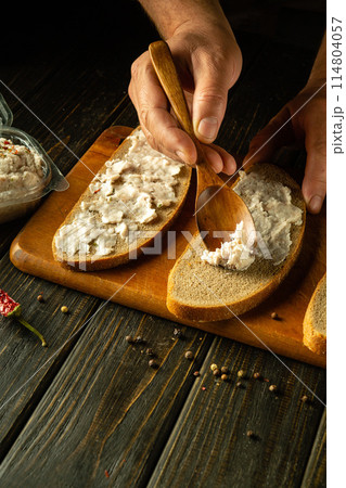 Chef hands spread lard on rye bread with a wooden spoon for making sandwiches on a kitchen board. Place for advertising Chef hands spread lard on rye bread with a wooden spoon for making sandwiches on a kitchen board. Place for advertising 114804057