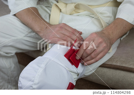 Karateka fixes knee protector on his leg before competition 114804298