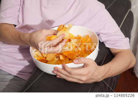 Caucasian person in pink t-shirt holding plate full of potato chips and preparing to eat 114805226