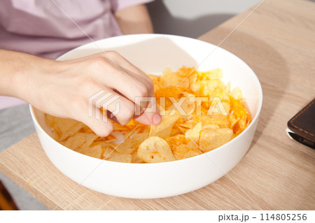 Caucasian person in pink t-shirt holding plate full of potato chips and preparing to eat 114805256