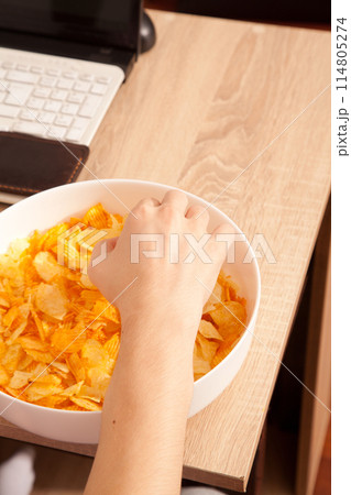 Potato chips in porcelain plate, caucasian man holding potato chips in hand, snack while working on laptop 114805274