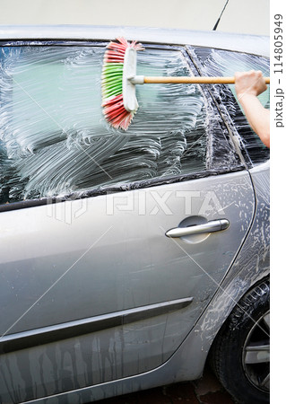 Caucasian male washing windows of dirty gray car with brush and soap suds, car washing with brush Caucasian male washing windows of dirty gray car with brush and soap suds, car washing with brush 114805949