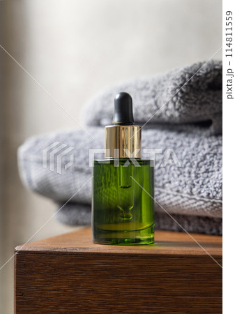 Green dropper bottle near grey folded towels on wooden countertop in bathroom, mockup Green dropper bottle near grey folded towels on wooden countertop in bathroom, mockup 114811559