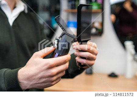 Barber holding combs and trimmer in the barbershop. 114811572