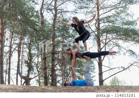 Three people standing in an elaborate acro yoga pose. 114813281