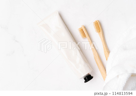 Top view of white metal tube without label and toothbrushes on white background 114813594