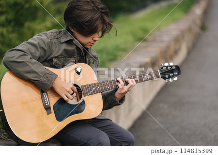 Portrait of handsome teenage boy playing guitar outdoor. Boy using classic guitar. Male alone making music Portrait of handsome teenage boy playing guitar outdoor. Boy using classic guitar. Male alone making music 114815399