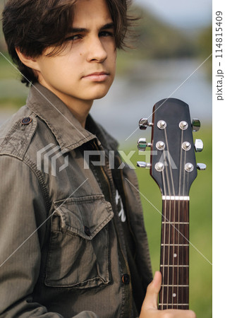 Fashion portrait of long hair boy hold acoustic guitar. Young boy preparing for playing guitar outdoor 114815409