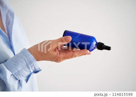 Female hands in a blue shirt hold a blue bottle of serum. Female hands in a blue shirt hold a blue bottle of serum. 114815599