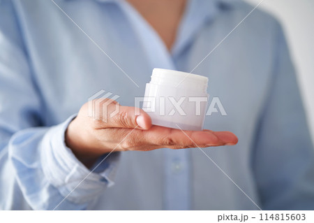 Hands in a blue shirt hold a jar of cream. 114815603