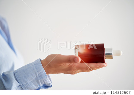 Female hands in a blue shirt hold a pink bottle of serum. Female hands in a blue shirt hold a pink bottle of serum. 114815607