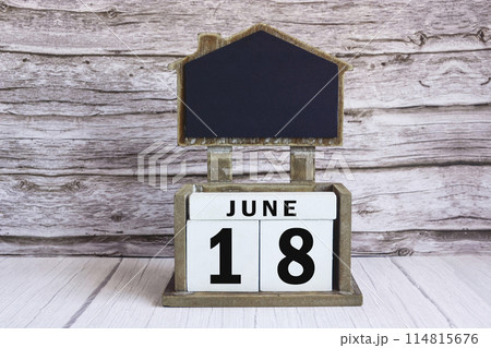 Chalkboard with June 18 date on white cube block on wooden table. 114815676