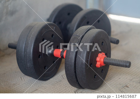 Pair Of Black Dumbbells On Gym Floor Near Concrete Wall In Daylight 114815687