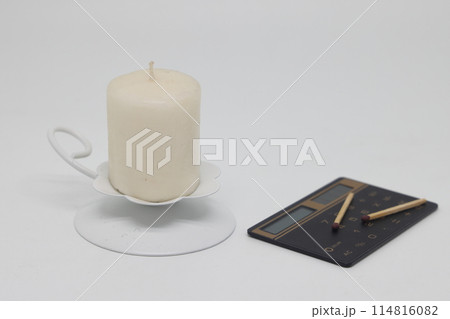 A candle in a white candlestick and matches on a calculator, is it worth it to burn. 114816082