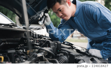 Car mechanic repairer analyzing car problems with an electric lamp while working on the cradle. Side view of expert technician repairing a car in the workshop. Car mechanic repairer analyzing car problems with an electric lamp while working on the cradle. Side view of expert technician repairing a car in the workshop. 114818427