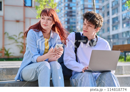 Teenage college students guy and girl talking, sitting outdoor near educational building 114818774