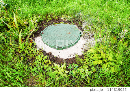 Covered sewer manhole with green plastic cover, sewage system. Sewerage networks. Sanitary sewer system manhole cover Covered sewer manhole with green plastic cover, sewage system. Sewerage networks. Sanitary sewer system manhole cover 114819025