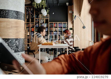 Selective focus side view shot of Middle Eastern boy and Asian girl sitting at table in college library doing homework or preparing for test 114819270