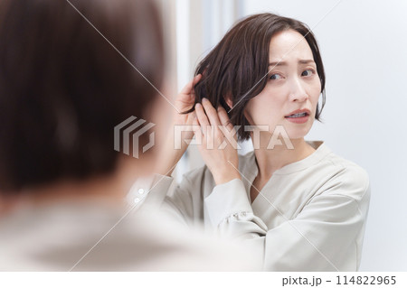 鏡を見て髪の毛を触るミドル女性（美容・ヘアセット・ヘアケア・髪の毛） 114822965
