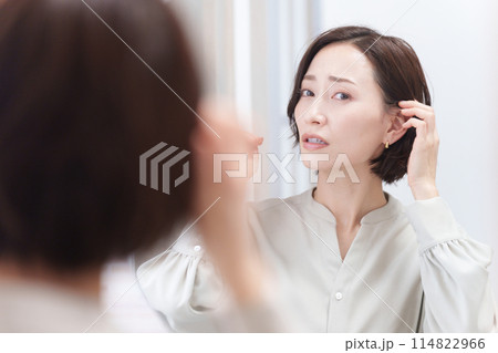 鏡を見て髪の毛を触るミドル女性（美容・ヘアセット・ヘアケア・髪の毛） 114822966