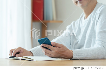 スマホと手帳をチェックするミドル男性 114825312