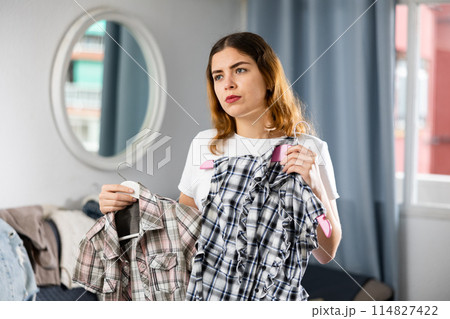 Young woman chooses what shirt to wear in the interior of house 114827422