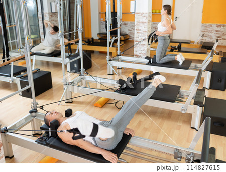 Man works out in gym and performs set of exercises to stretch leg muscles with help of reformer 114827615