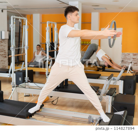 Guy performing pilates exercises with resistance ring on reformer 114827894