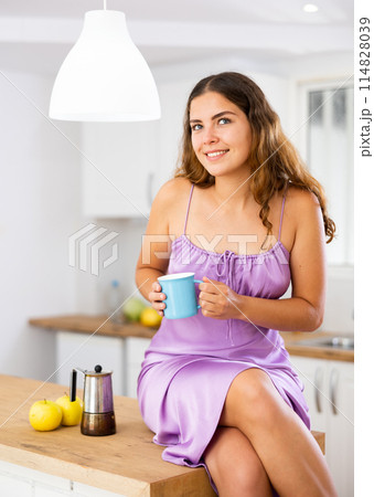 Attractive girl with cup of coffee in her hands posing on kitchen table Attractive girl with cup of coffee in her hands posing on kitchen table 114828039