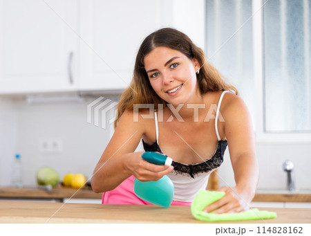 Positive housewife cleans table in home kitchen 114828162