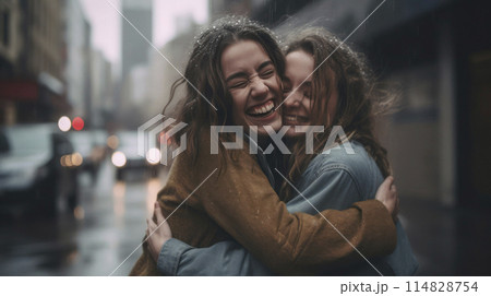 Two Caucasian happy young women hugging under the rain in the street in summer, selective focus. 114828754