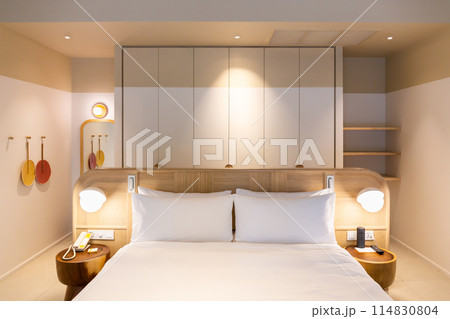 White bed and pillows in a room with decorative plants and warm lighting. 114830804